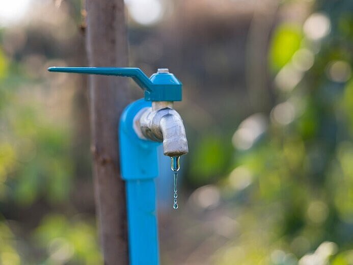 Blauer, tropfender Wasserhahn im Garten